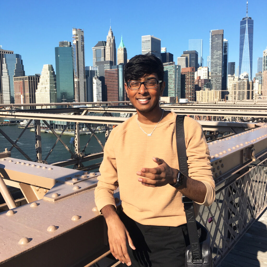 NC State student Kiran Soma standing on the Brooklyn Bridge with the lower Manhattan skyline in the background.