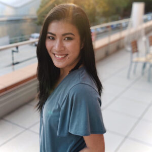 A headshot of LilyGrace Wolfe who is an Asian female in her 20s. She has long black hair, is smiling, and is wearing a light blue t shirt.