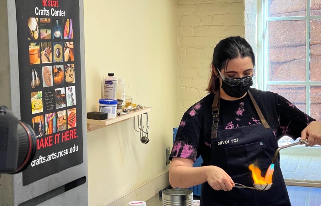 Social media influencer Sofia Nygaard in the jewelry studio at the NC State University Crafts Center, using a torch to melt old jewelry pieces for new use.