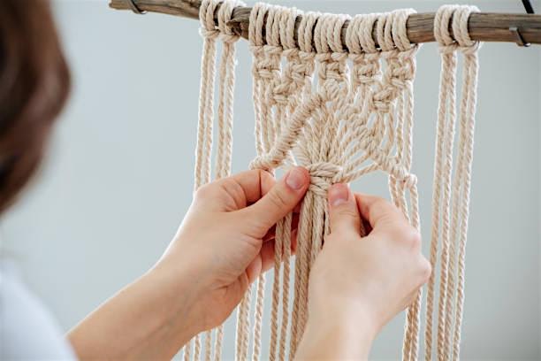 A person ties knots in yarn to create a macrame pattern